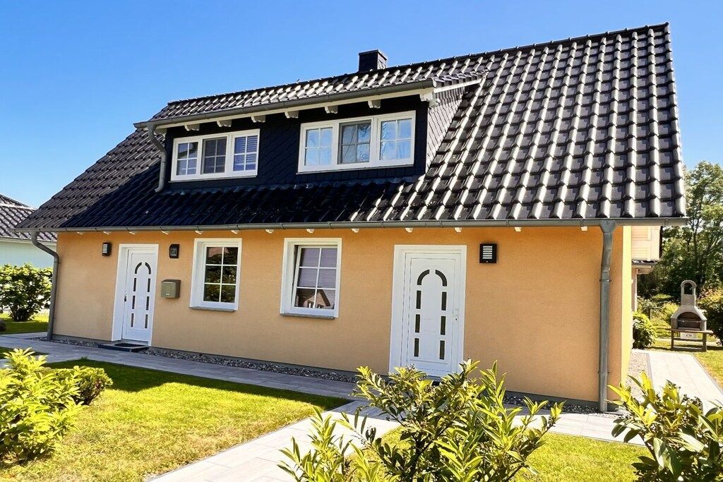 Ein zweistöckiges Haus mit Ziegeldach, einer Veranda und einem gepflegten Rasen.