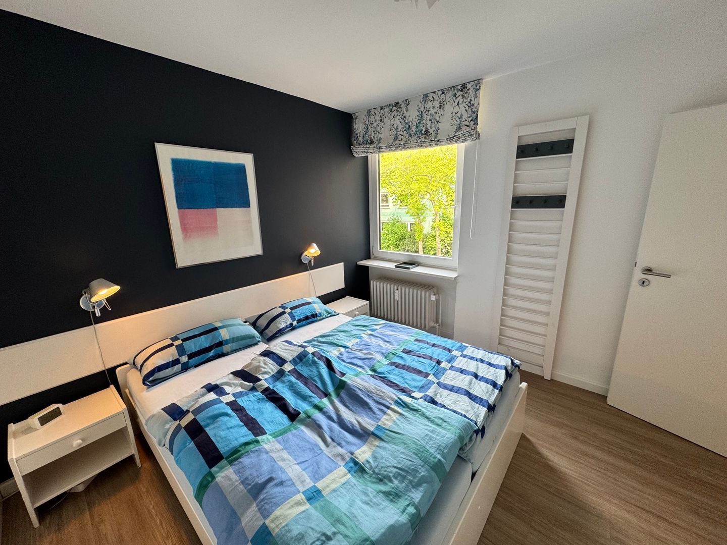 Une chambre à coucher avec un lit, des lampes de chevet, une fenêtre donnant sur un beau paysage et une porte.