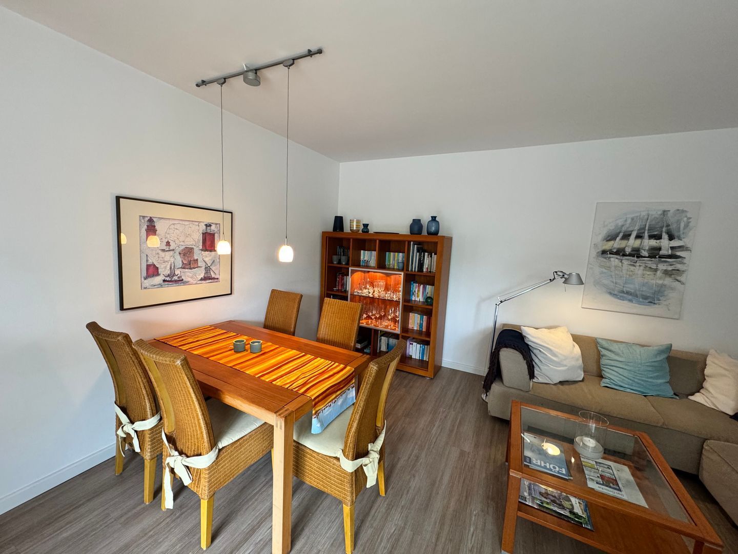 Un coin repas avec une table en bois et des chaises en osier, une bibliothèque, un canapé et une table basse avec des magazines.