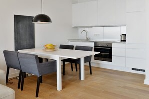 A modern kitchen with white cabinets, a black oven, and a dining area with a white table and grey chairs. - Holiday apartment with 2 bedrooms (Sassnitz)