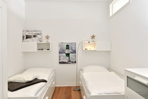 A small, white room with two beds, a floor lamp, and artwork on the walls. - Holiday apartment with 2 bedrooms (Sassnitz)