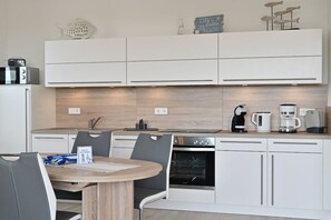 A modern kitchen with white cabinetry, a built-in oven, and a coffee maker. - The sea is always a good idea! (Glowe)
