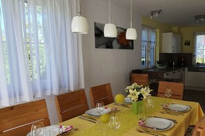Ein Essbereich mit einem Tisch für vier Personen, Stühle, einer Blumenvase und einer Küche im Hintergrund.