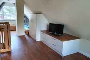 Una habitación con una televisión sobre un mueble de madera, un armario blanco y suelo de madera.