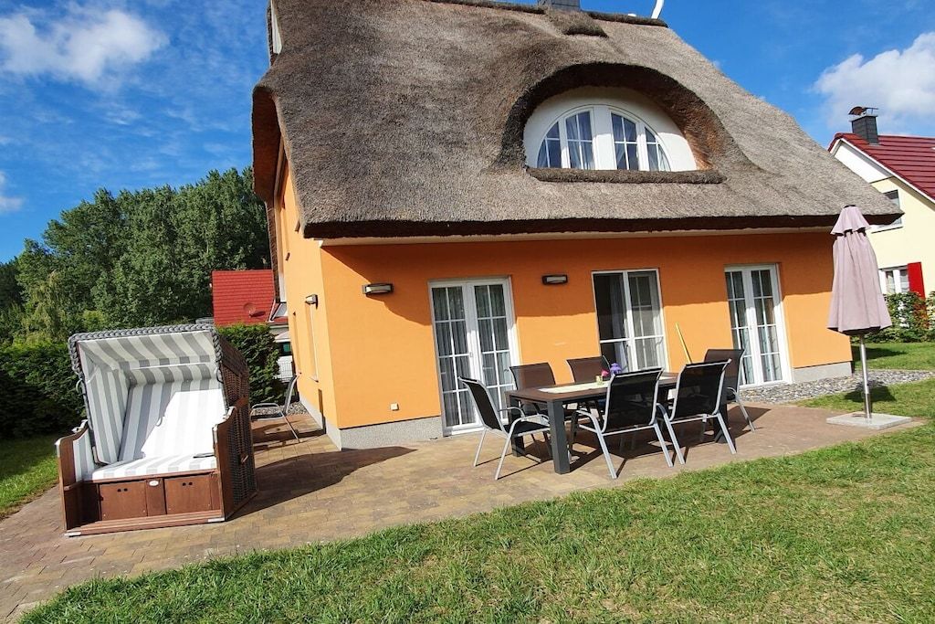 A house with a thatched roof, an orange exterior, and a patio with outdoor furniture.