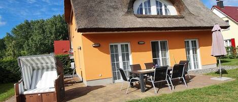 A house with a thatched roof, an orange exterior, and a patio with outdoor furniture.