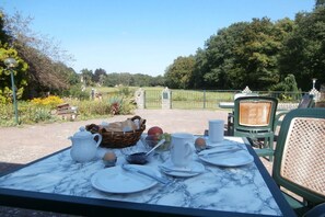 An outdoor dining table set with plates, cups, and a basket of bread, overlooking a garden with a fence and trees. - Country House Lake District 2 (Lychen)