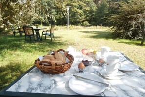 An outdoor dining table set with plates, cups, and a basket of bread, surrounded by chairs and greenery. - Country House Lake District 2 (Lychen)