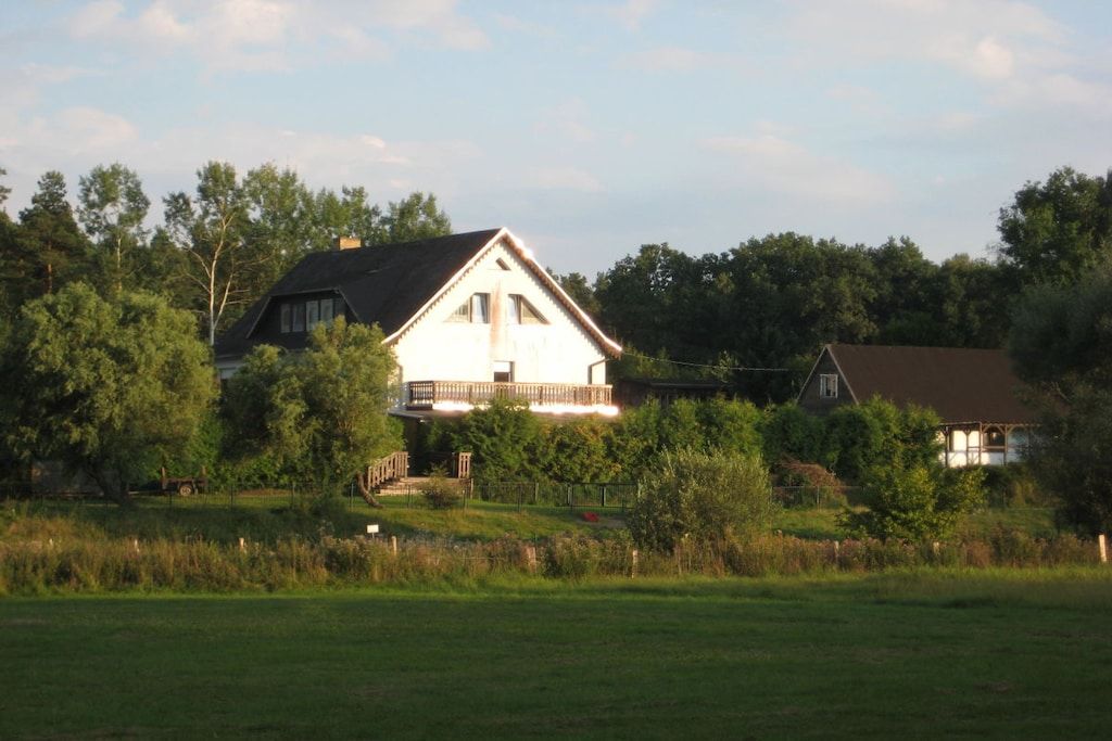 Ein zweistöckiges Haus mit Balkon, umgeben von Bäumen und einer grünen Wiese.