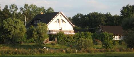 Ein zweistöckiges Haus mit Balkon, umgeben von Bäumen und einer grünen Wiese.