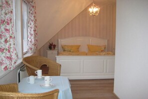 A bedroom with a bed, a table with cups, a chair, and a window with floral curtains. - Country House Lake District 2 (Lychen)