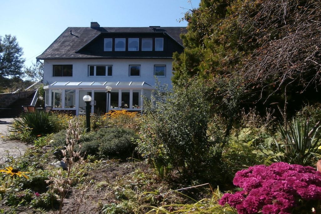 A two-story house with a covered porch and a garden with various plants and flowers.
