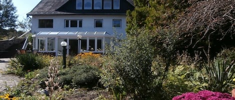 A two-story house with a covered porch and a garden with various plants and flowers.