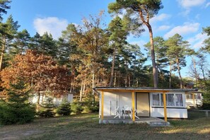 A small cabin with a porch and two chairs, surrounded by trees and a clear sky. - Holiday Park Lakeland 2 (Lychen)