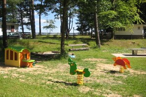 A playground with a slide, swings, and a small playhouse. - Holiday Park Lakeland 1 (Lychen)