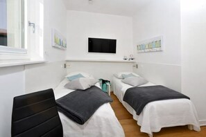Una habitació amb dos llits individuals, una televisió plana penjada a la paret i obres d'art a les parets.