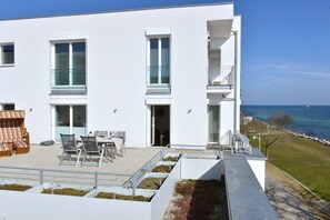 Een modern gebouw met twee verdiepingen, een balkon, terras en uitzicht op zee.