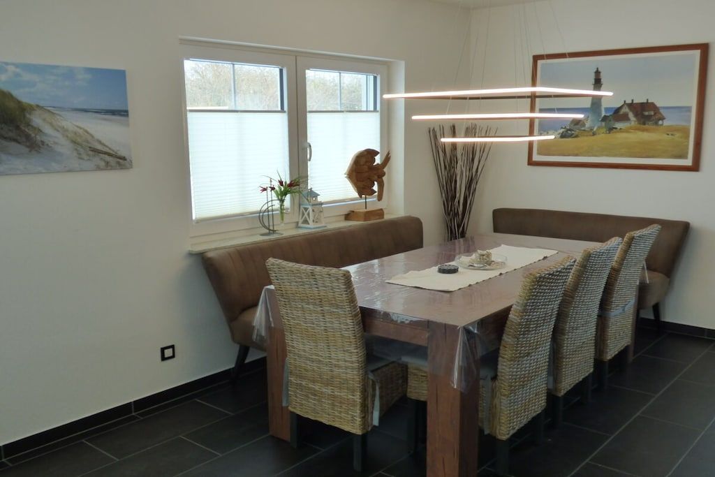 Un coin repas avec une table en bois, des chaises en osier, un banc et des œuvres d’art accrochées aux murs.