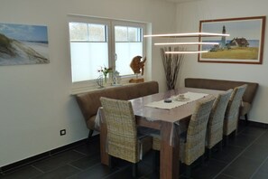 Ein Essbereich mit einem Holztisch, Korbstühlen, einer Bank und Kunstwerken an den Wänden.