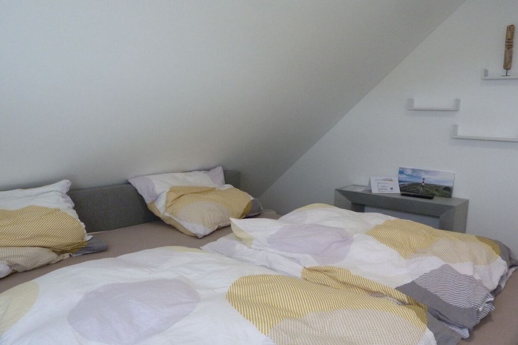 A bedroom with two beds, a bedside table, and a wall-mounted shelf.