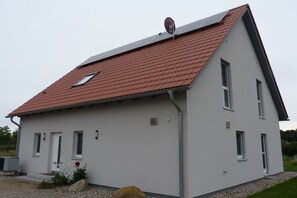 Een herenhuis met een rode dakbedekking, een schotelantenne en een kleine tuin met een rots en bloemen.