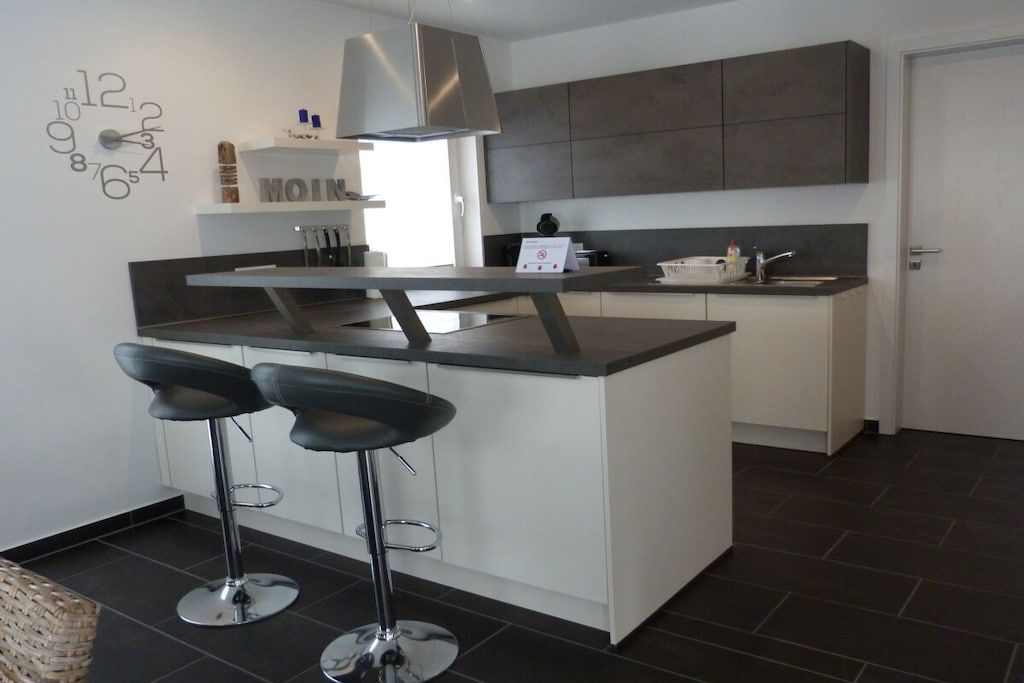 A modern kitchen with a central island, two bar stools, and a stainless steel range hood.