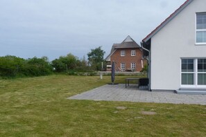 Ein Wohngebäude mit gepflasterter Terrasse, einer Bank und einer Skulptur.