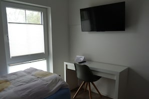 Ein Schlafzimmer mit einem Bett, einem Schreibtisch, einem Stuhl und einem an der Wand befestigten Fernseher.