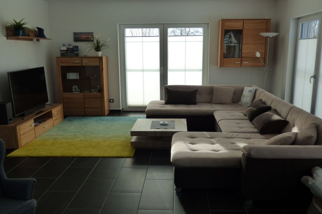 Ein Wohnzimmer mit einem Ecksofa, einem Flachbildfernseher, einer Holzkabine und einer Schiebeglastür.