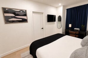 Habitación de hotel con cama, televisor de pantalla plana, espejo, escritorio con lámpara y ventana con cortinas.