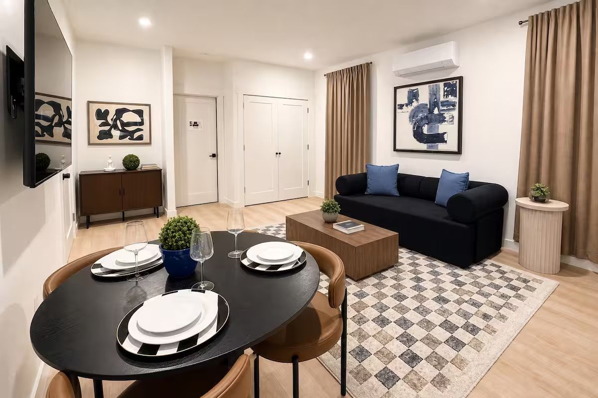 A modern living room with a black sofa, a coffee table, and a dining area with a round table set for four.