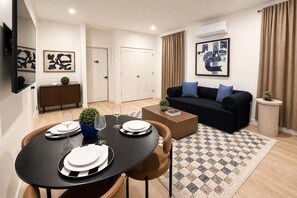 A modern living room with a black sofa, a coffee table, and a dining area with a round table set for four.