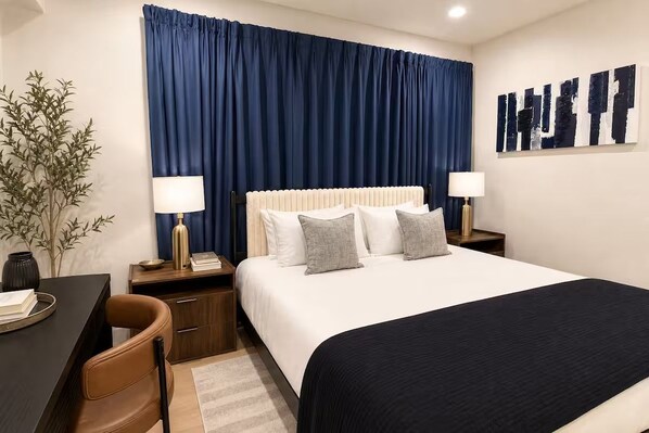 A hotel room with a bed, two bedside tables, a desk, a chair, and a large window with curtains.