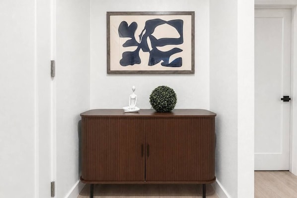 A room with a wooden cabinet, a framed abstract painting, and a small potted plant.