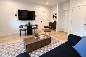 A modern living room with a flat-screen TV, a round dining table, and a sofa.