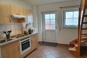 A compact kitchen with a stove, oven, and sink. There is a door with a window above it, and a small step leading to a wooden staircase. - 2 in Vanessa's house (Zingsst)