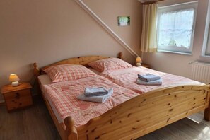 Quarto com cama de madeira, duas mesas de cabeceira com abajures, uma janela com cortinas e um radiador.