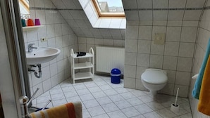 Kylpyhuoneessa on kattovalokuvio, valkoinen pesuallas, wc-istuin ja sininen roskakori.