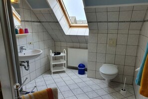 A bathroom with a skylight, a white sink, a toilet, and a blue trash bin. - 2 in Vanessa's house (Zingsst)