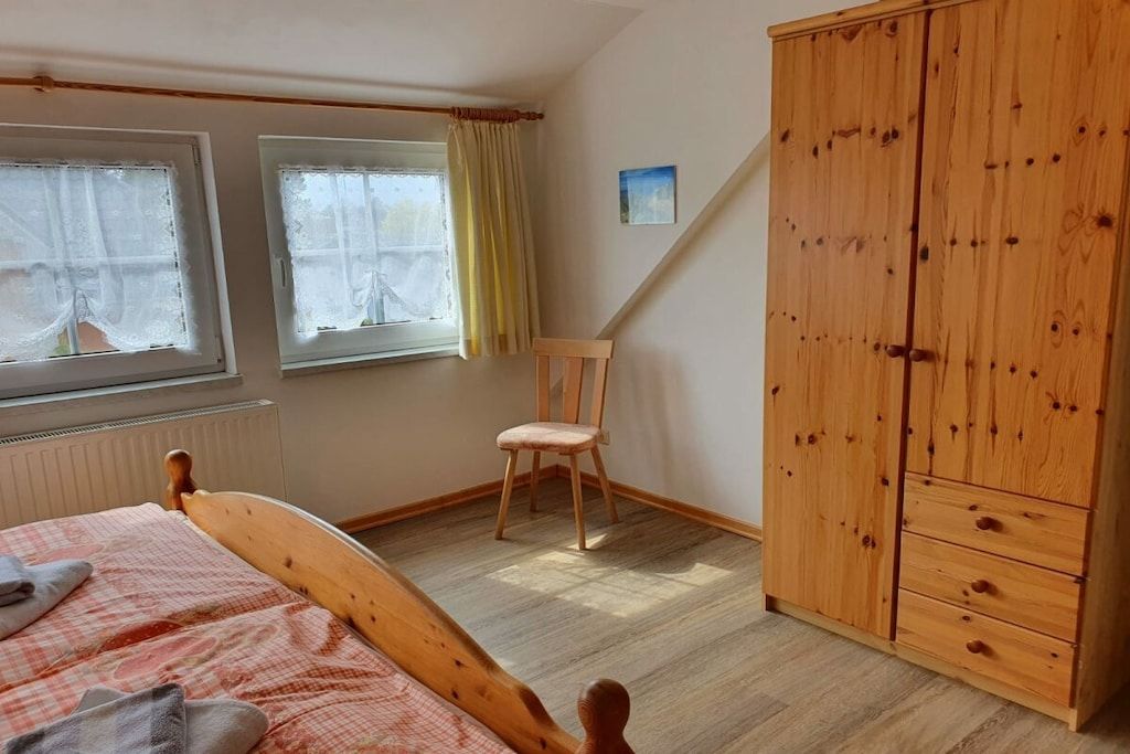 Una camera da letto con un letto in legno, due finestre con tende, un armadio in legno e una sedia.