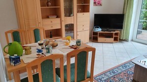 Ruokailutila, jossa on kahdelle katettu ruokapöytä, televisio ja kirjahylly.