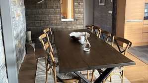 Een eetgedeelte met een lange houten tafel, zes stoelen, een zwart hanglamp en een stenen muur.