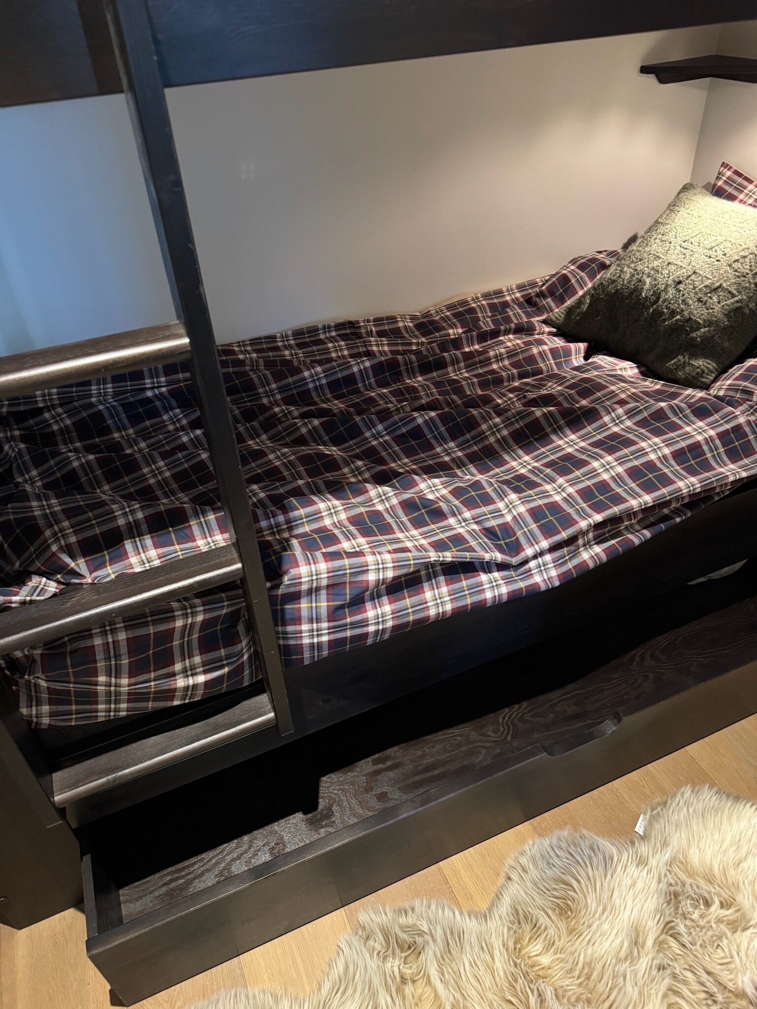 A bunk bed with a plaid bedspread and a single pillow.