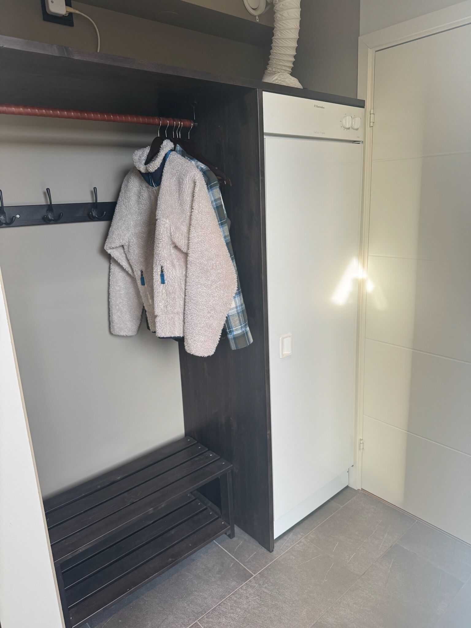 A compact room with a built-in wardrobe, a bench, and a white appliance.