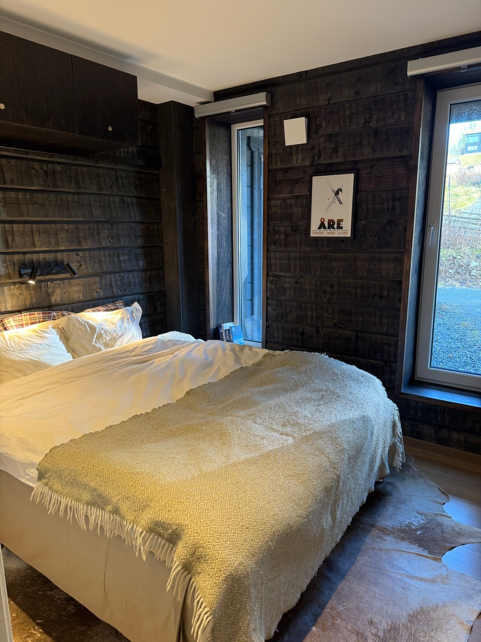 A bedroom with a large bed, dark wooden walls, a window, and a framed picture on the wall.