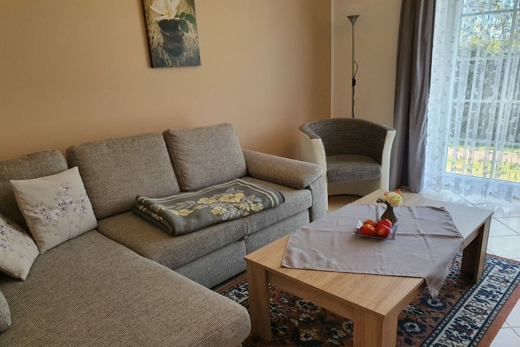 Ein Wohnzimmer mit einer Couch, einem Sessel, einem Couchtisch und einem Fenster mit Vorhängen.