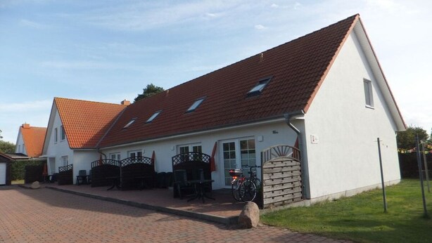 A two-story house with a red-tiled roof, a paved driveway, and a front porch with outdoor furniture. - 5 in the Damaris house (Zingst)