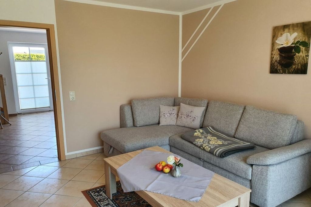 A living room with a grey sofa, a small wooden table with a vase of flowers, and a painting on the wall.