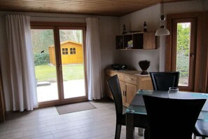 Comedor con mesa, sillas, un armario y vista a una cabaña de madera a través de un vidrio.