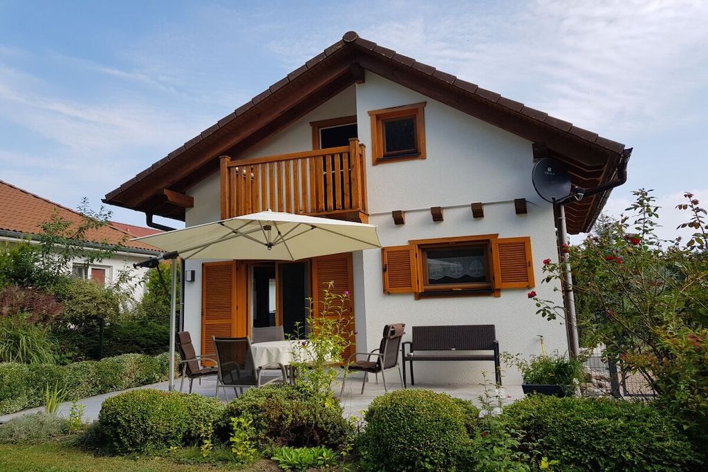 A two-story house with a balcony, a patio with chairs and an umbrella, and a satellite dish.